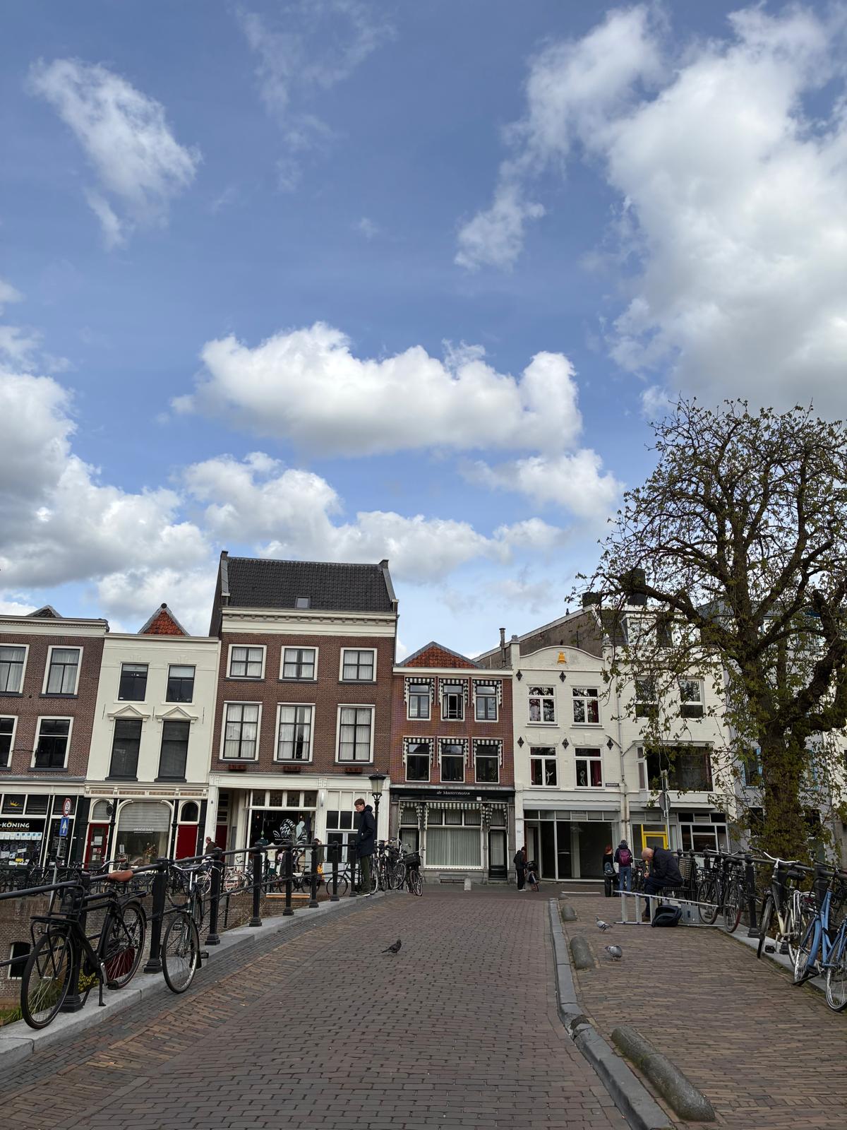 Cobblestone bridge over the Oudegracht in Utrecht with historic canal houses, parked bicycles and a bright cloudy sky